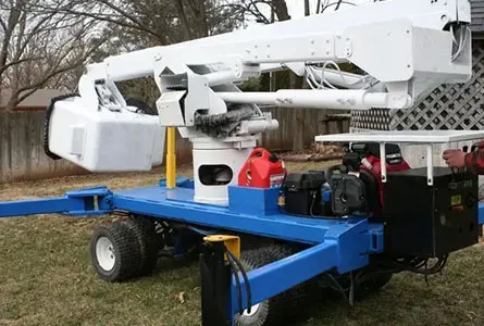 A compact, mobile aerial work platform on a wheeled base, featuring an extendable hydraulic arm and bucket for elevated access tasks, positioned outdoors on grass.